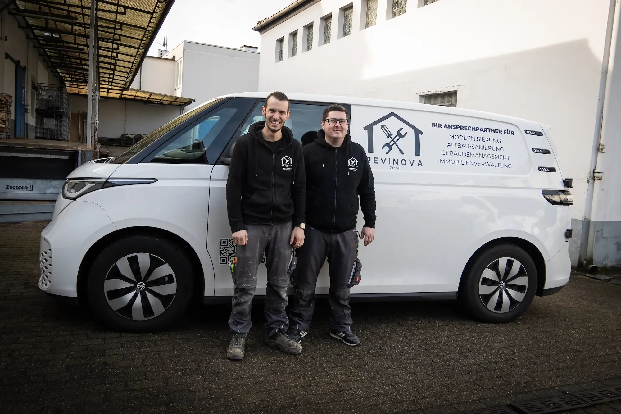 Lukas Vincenz und Benjamin Rechenbach vor einem Firmenwagen auf Ihrem Firmengelände.